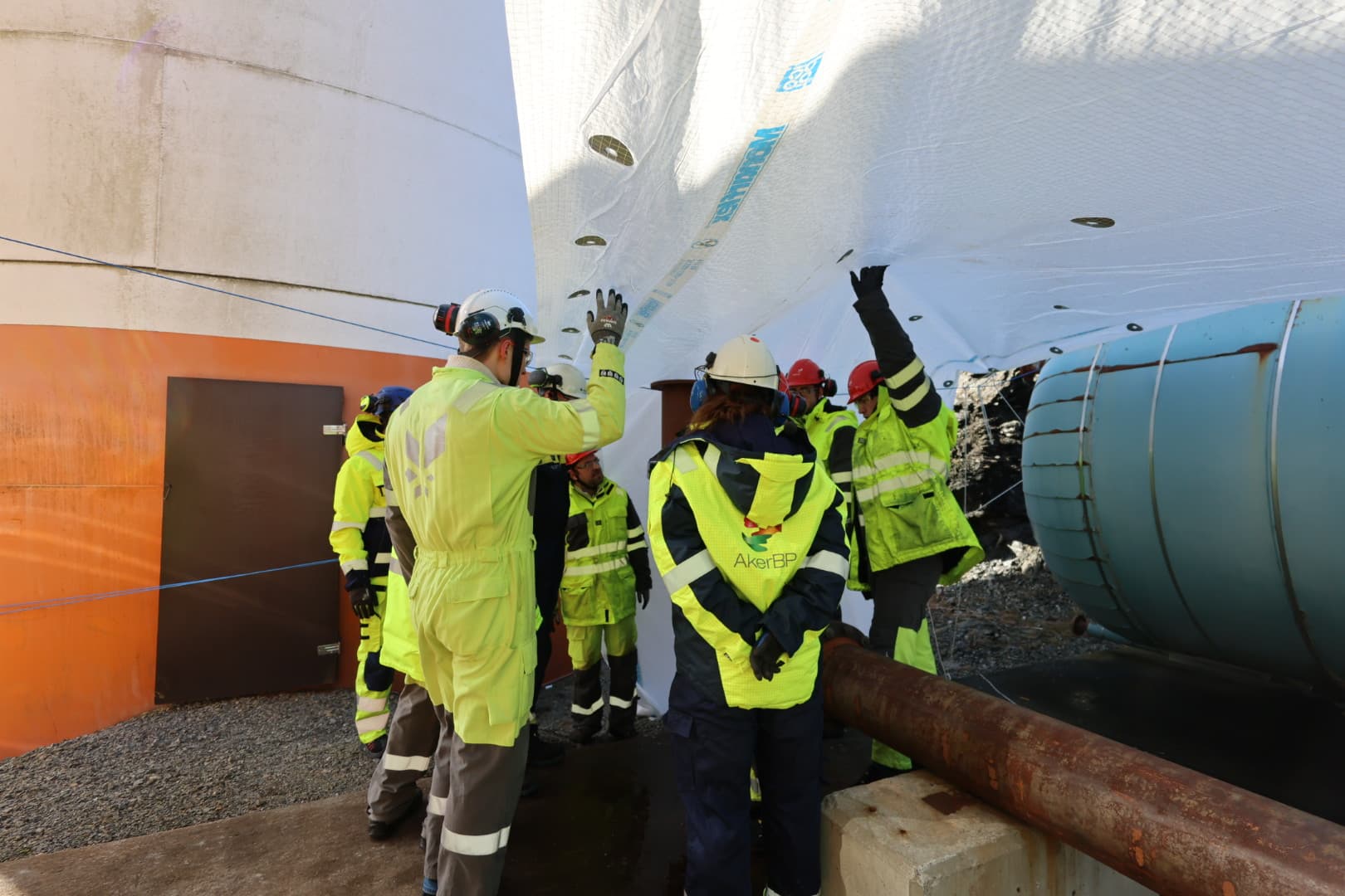 Field crew rigging insulation cladding around a tank and pipework on site